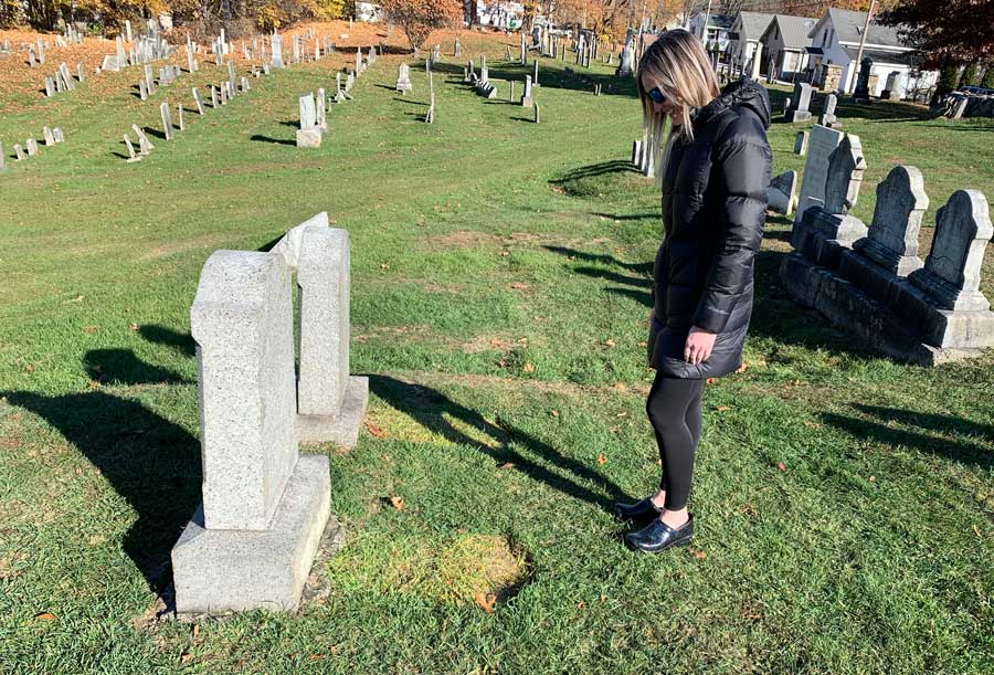 Assistant Town Clerk Kayla views a re-set gravestone.